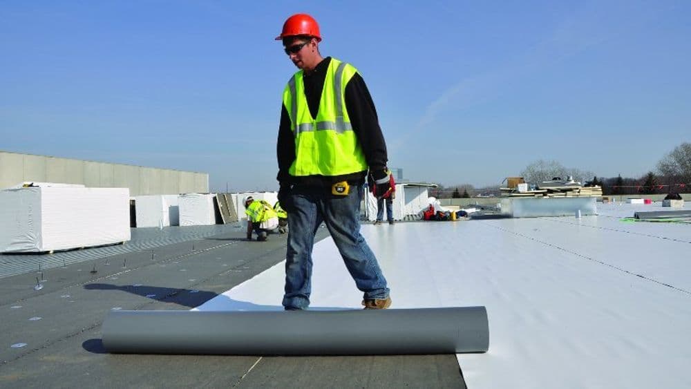 Construction worker installing a roofing membrane on a commercial building's flat roof.