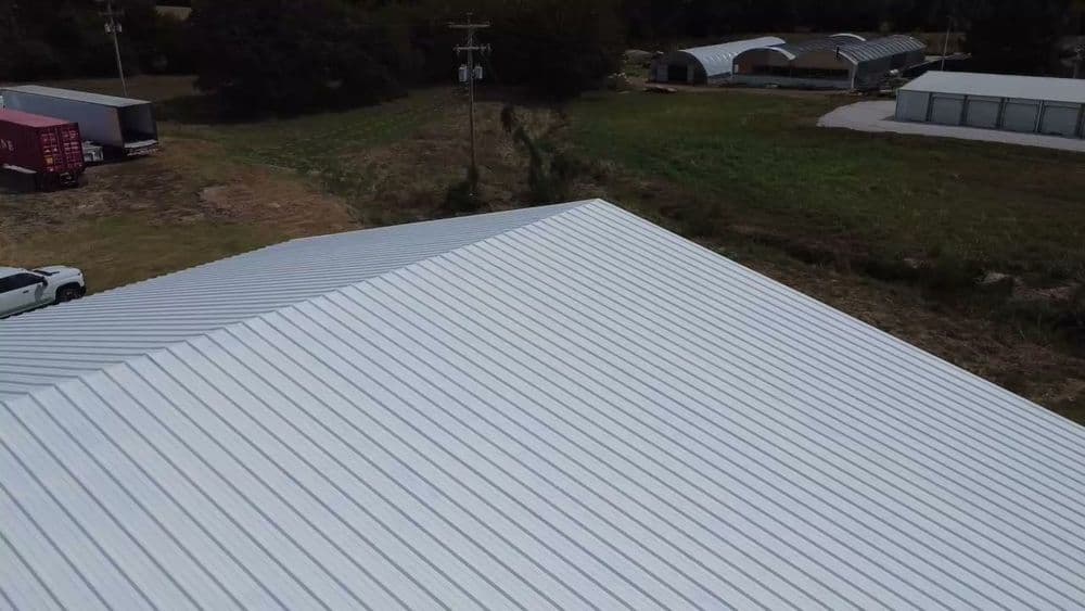 Aerial view of a metal roof on a building near agricultural structures and fields.