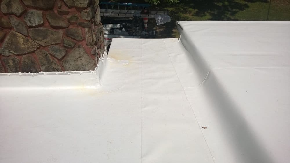 Flat roofing detail with a stone chimney, showing areas of sealing and potential wear.