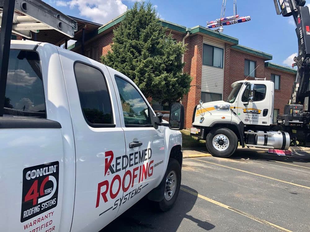 Redeemed Roofing Systems trucks at a residential building for roof installation services.