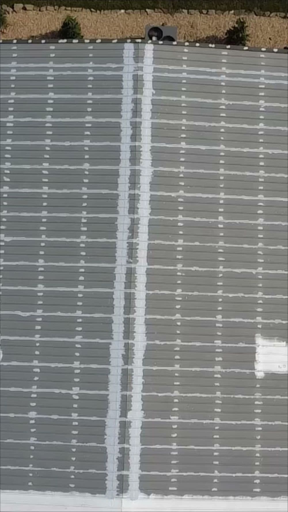 Aerial view of a gray rooftop with white seams and patches. Eco-friendly roofing solution.