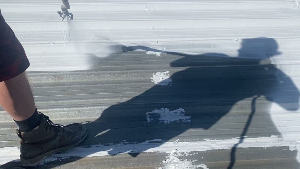 Person painting a metal roof while casting a shadow, showcasing renovation work.