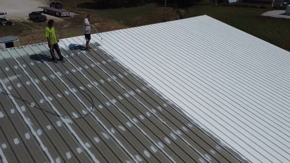 Workers applying white coating to a metal roof under clear skies.