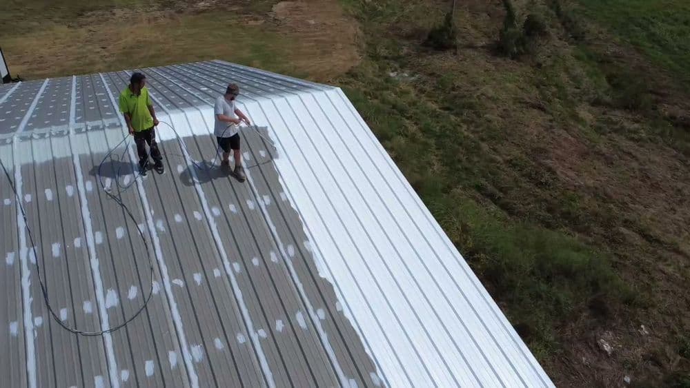 Workers applying roof coating on a metal roof, showcasing a repair project in progress.