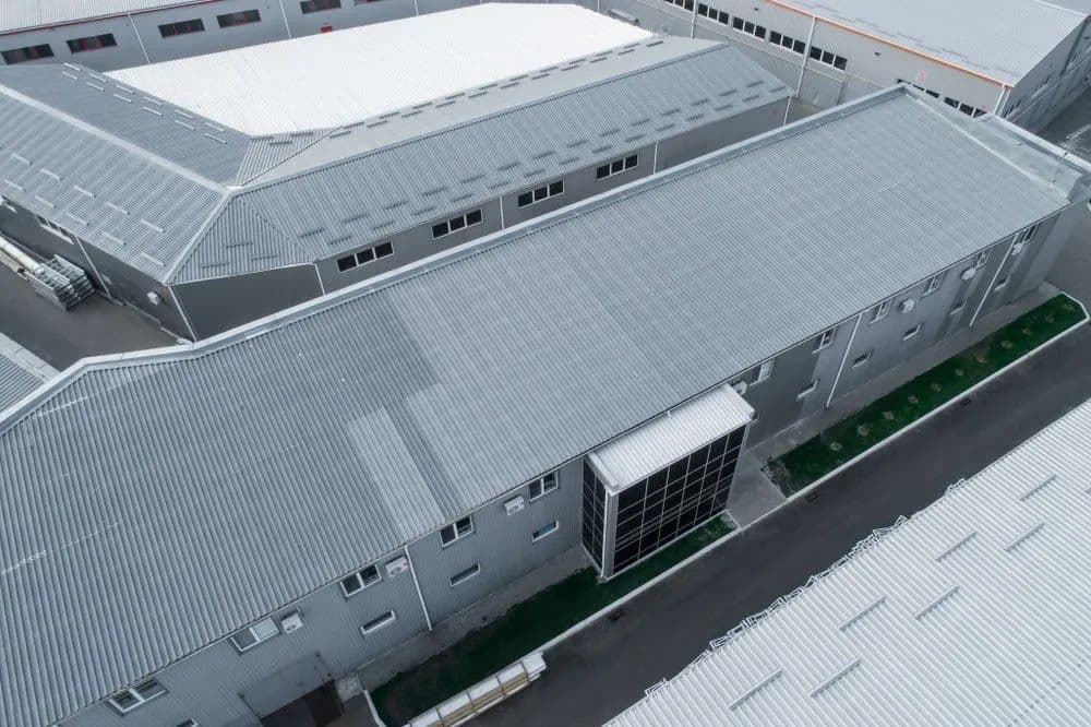 Aerial view of industrial building with gray roofs and central glass entrance.