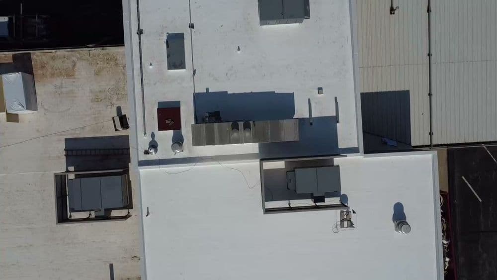 Aerial view of a flat commercial building roof with HVAC units and white coating.
