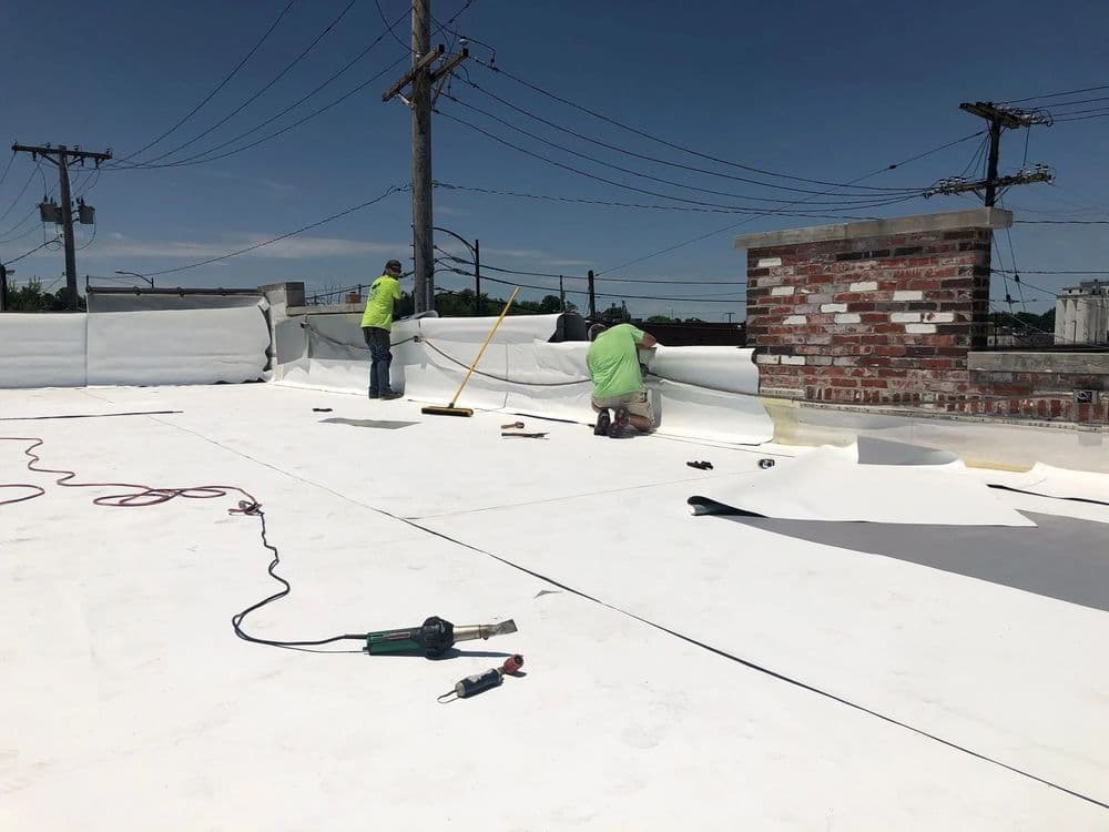 Workers applying roofing membrane on a commercial building rooftop under a clear blue sky.