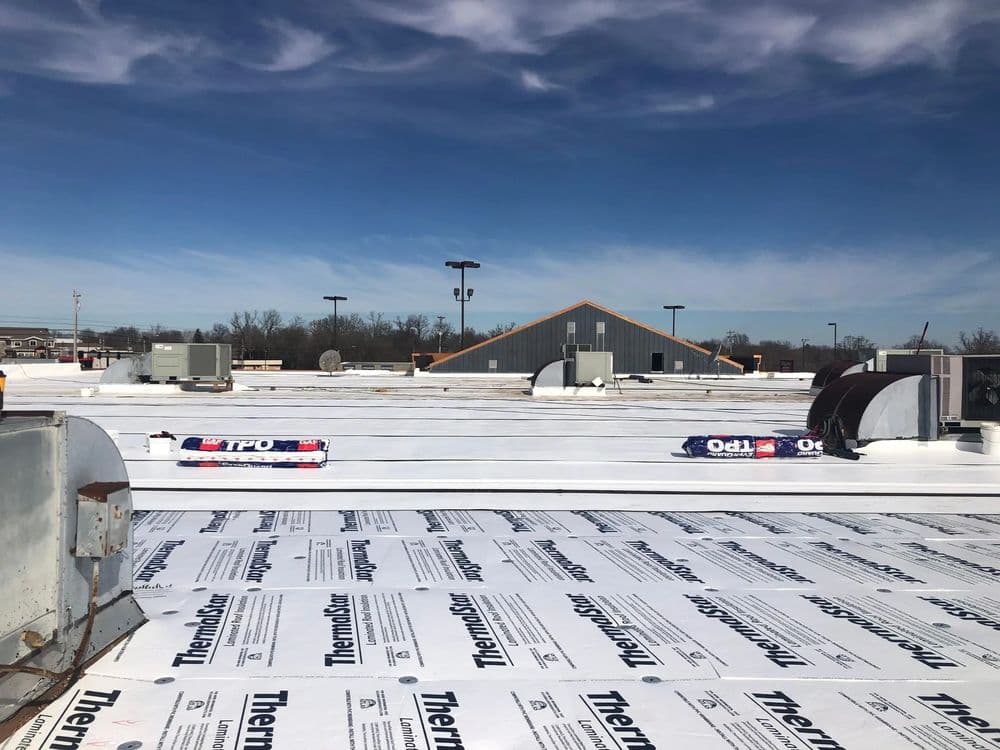 Flat commercial roof installation with white TPO membrane under a clear blue sky.