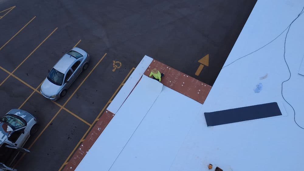 Aerial view of a worker in a yellow vest on a roof near parked cars and directional arrows.