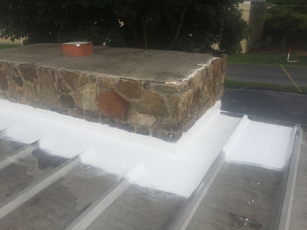 Chimney with stone base and white sealant on roof, showcasing waterproofing detail.