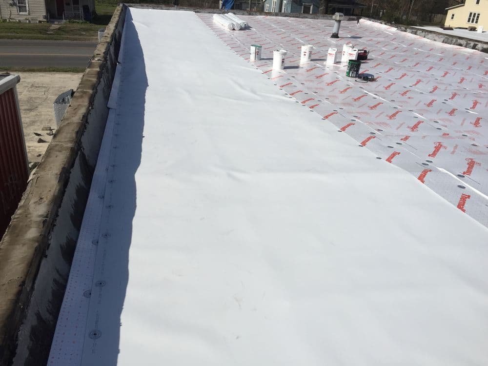 Flat roofing installation with white membrane and materials on a sunny day.
