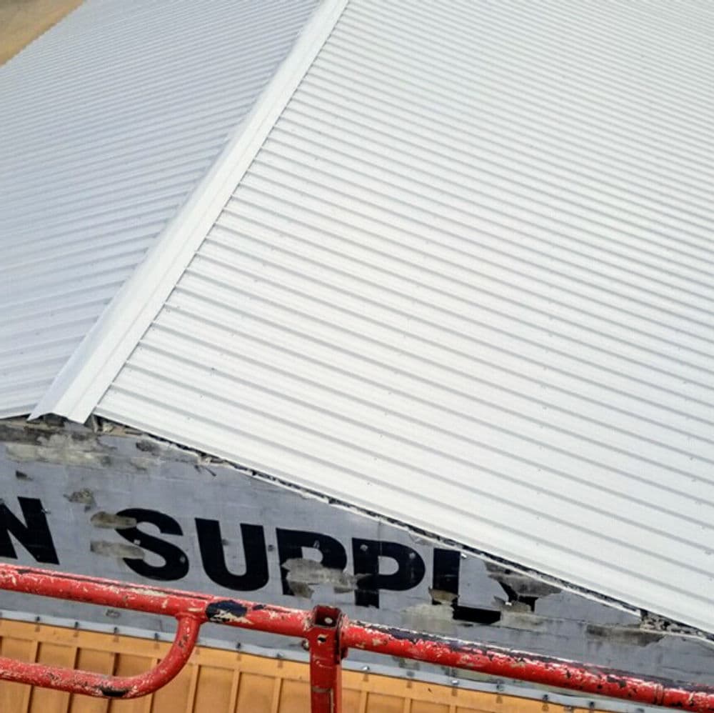 Metal roofing installation on a warehouse with scaffolding visible in foreground.