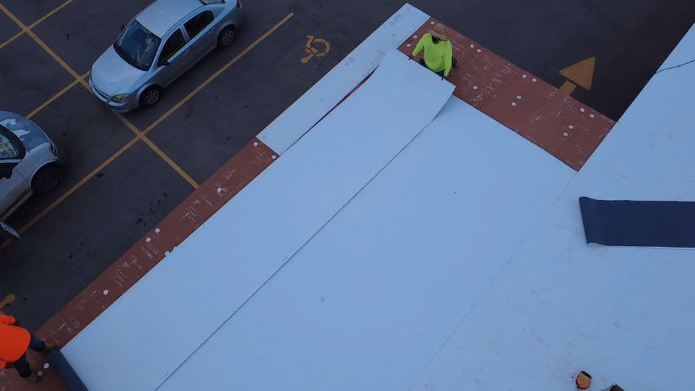 Roofing installation process with a worker laying white material over a building surface.