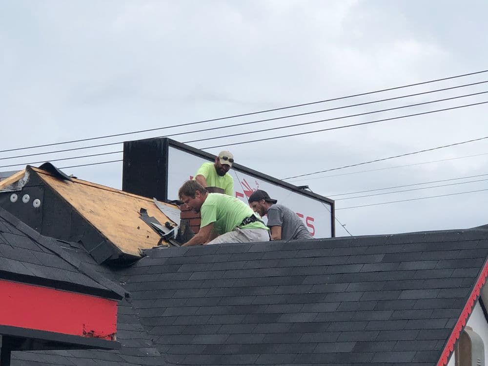 Roofers working on a building renovation, replacing shingles under a cloudy sky.