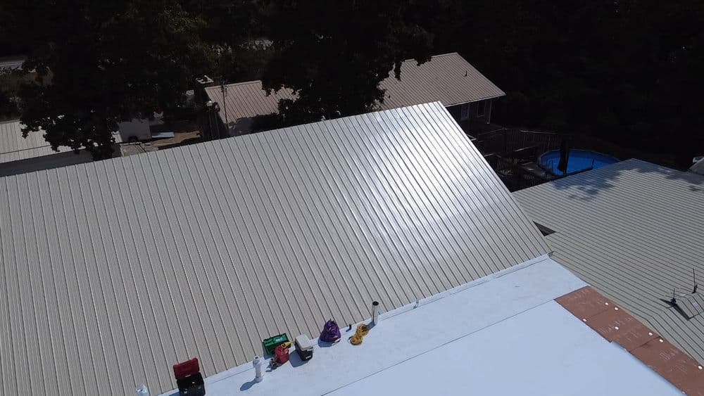Aerial view of a metal roof with tools and nearby houses and a pool in the background.