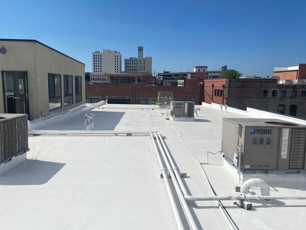 Roof view featuring HVAC units and city skyline in the background, clear blue sky.