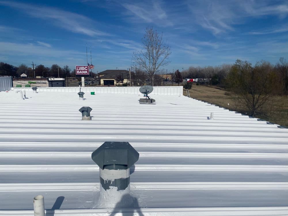 Flat white roof with vents and satellite dish, overlooking a bank and landscape.