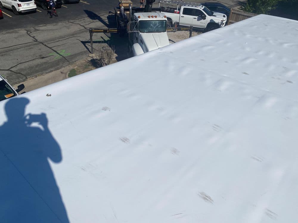 White rooftop view with a shadow, showing parked trucks and vehicles in the background.