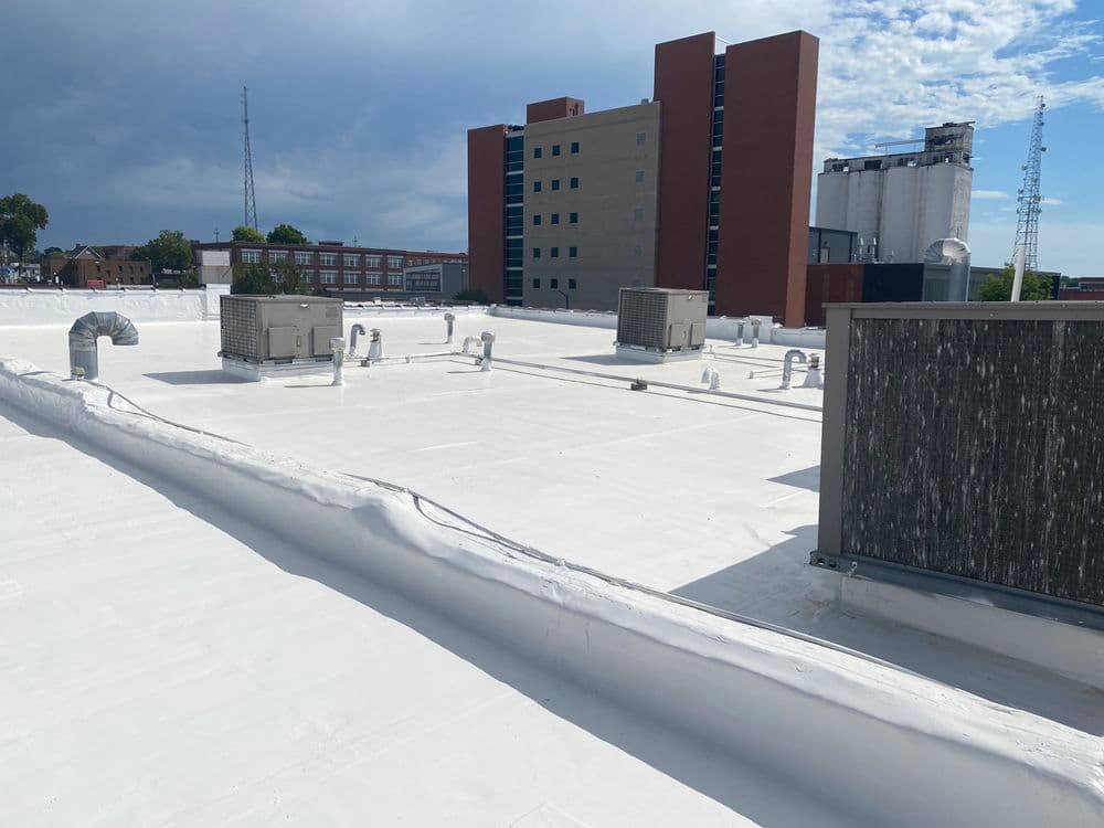 Flat roof with HVAC units and a white reflective coating, urban buildings in the background.