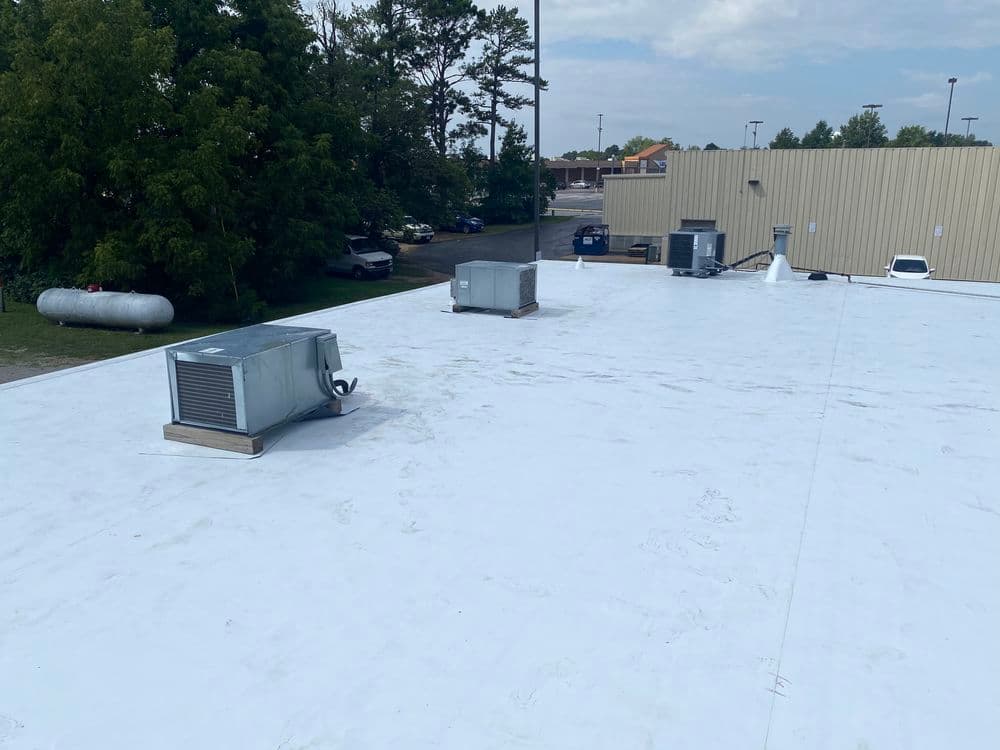 Flat commercial rooftop with HVAC units, trees in background, and clear sky overhead.