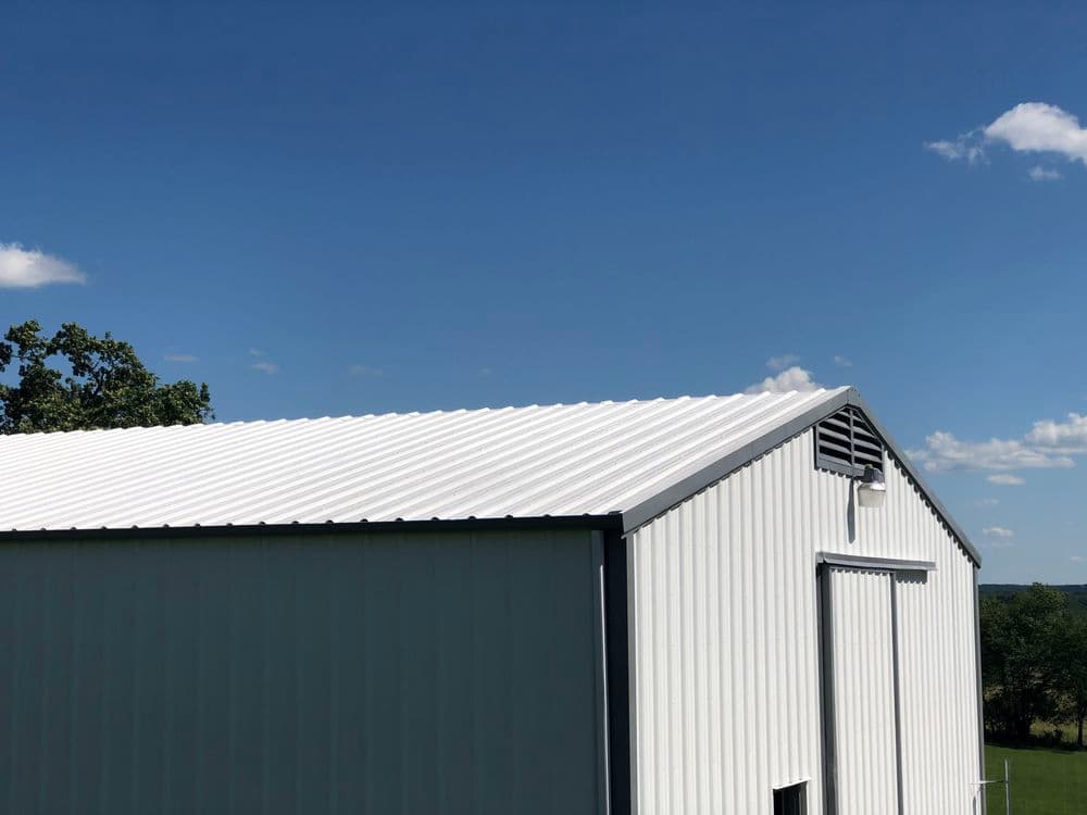 Metal warehouse building with a white roof under a clear blue sky.