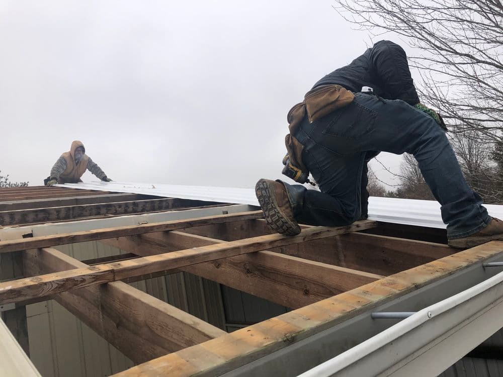 Two workers installing metal roofing on a residential building structure.
