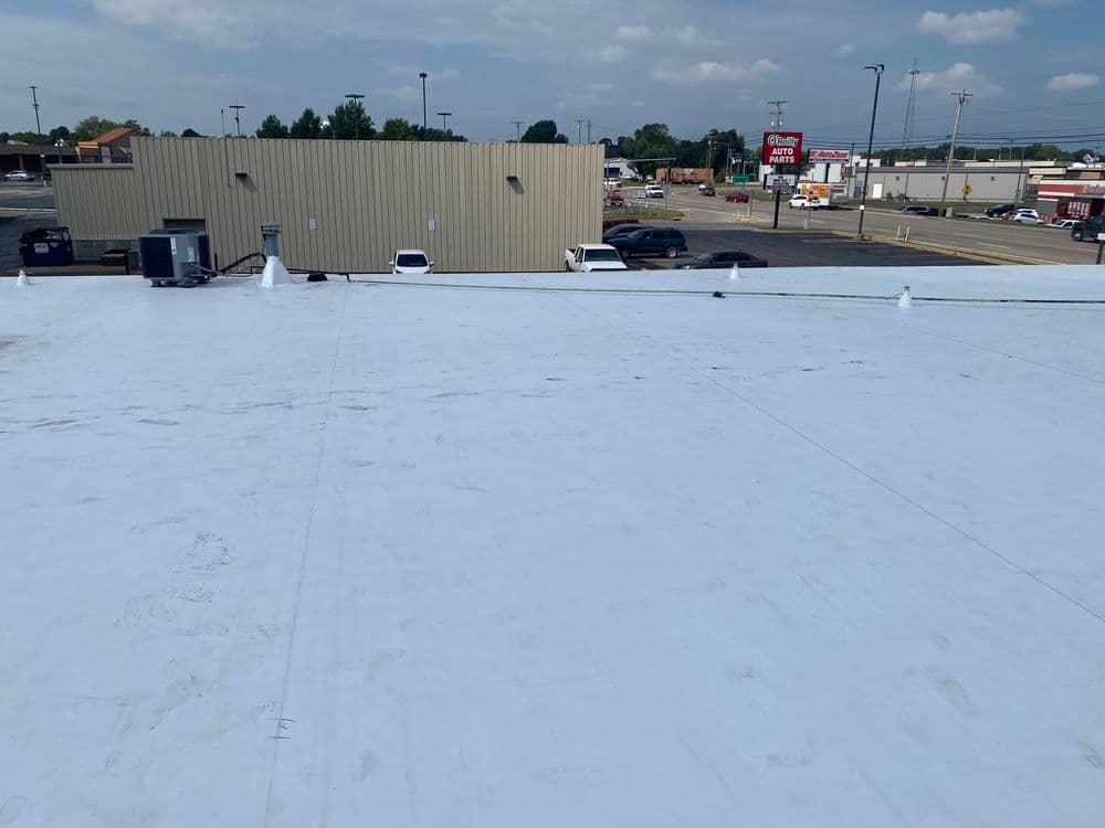 Flat commercial roof with white coating, surrounded by retail establishments and vehicles.