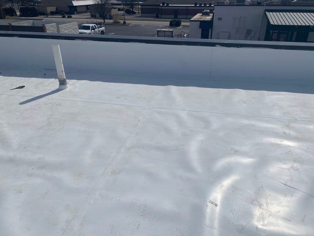 Flat commercial roof with white membrane and plumbing vent in sunny urban setting.