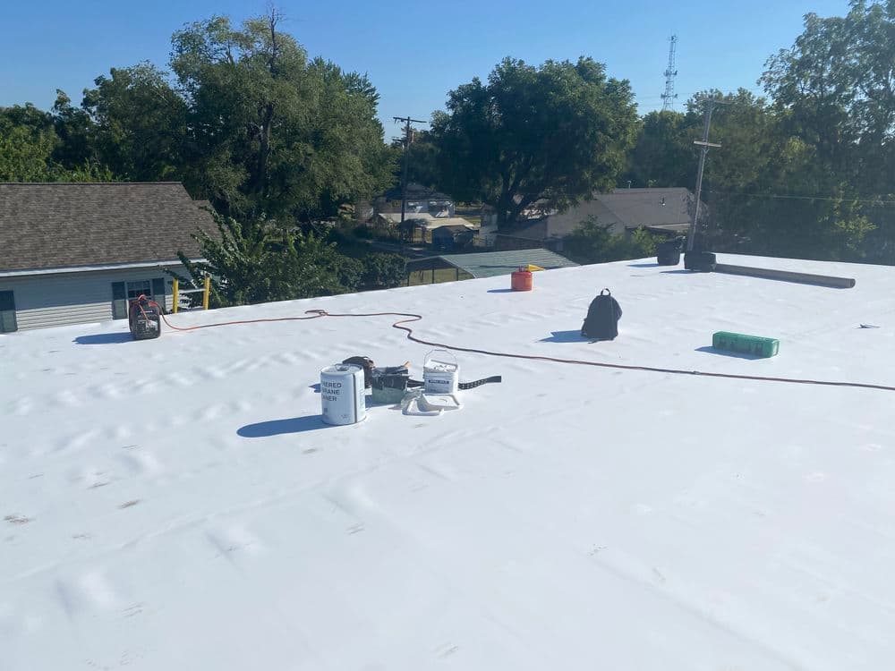 Flat white commercial roof under construction with tools, buckets, and a clear blue sky.