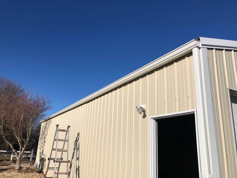 Metal building exterior with ladder, door, security camera, and clear blue sky.
