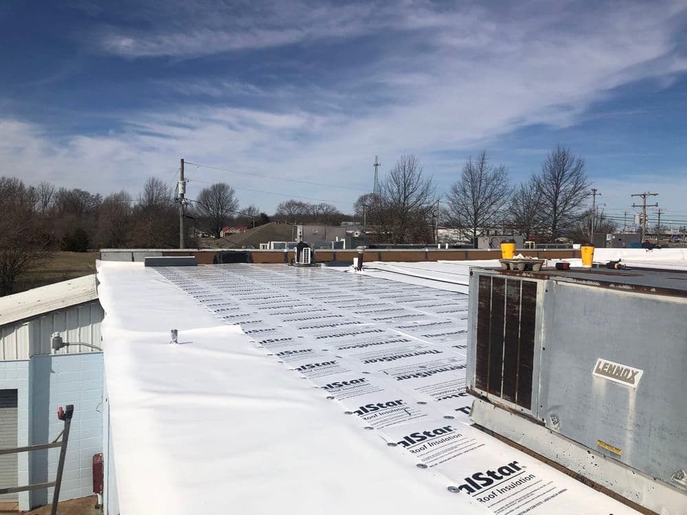 Newly installed white roofing material on commercial building under a clear blue sky.