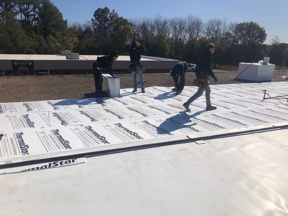 Workers installing thermal insulation sheets on a building rooftop under clear blue skies.