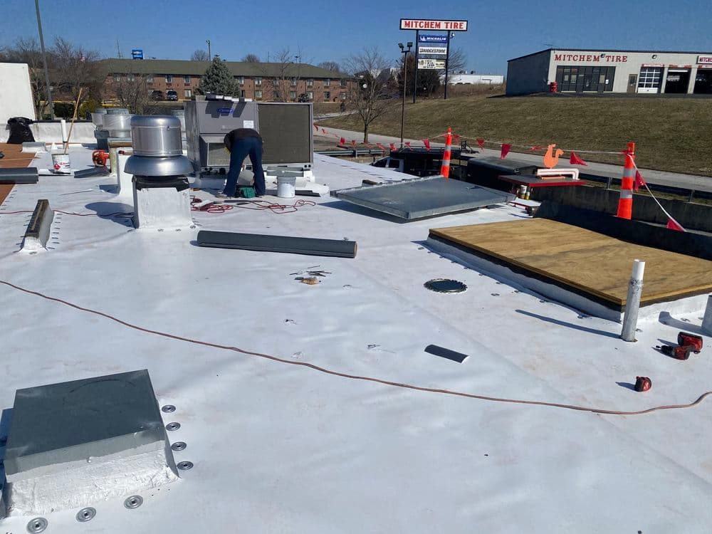 Roof construction site with workers, tools, and materials visible on a commercial building.
