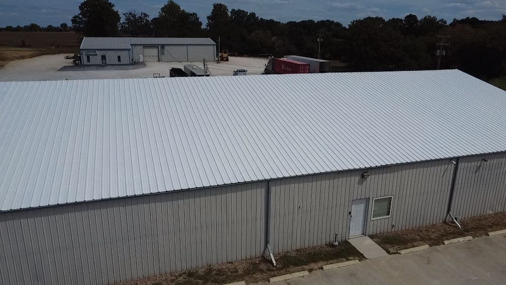 Aerial view of a large metal building with a white roof and surrounding industrial structures.