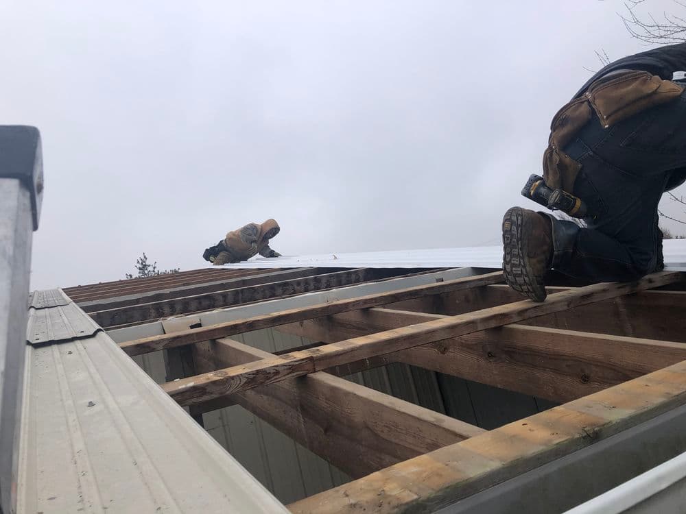 Roofing workers installing metal sheets on a residential roof under a cloudy sky.
