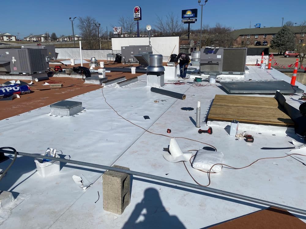 Workers installing roofing materials on a commercial building rooftop with HVAC units.