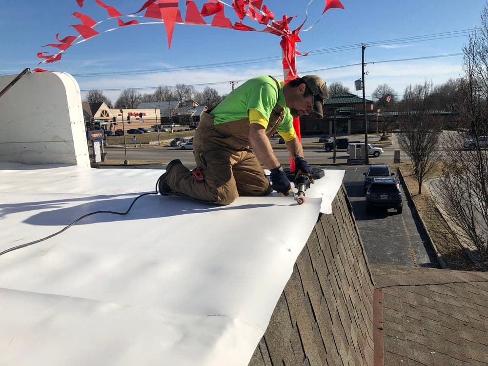 Roofer installing new roofing material on a commercial building under clear skies.