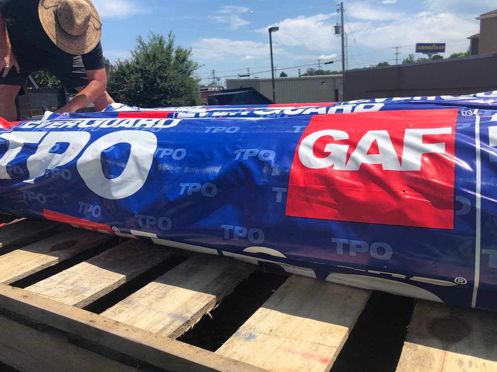 GAF TPO roofing membrane on wooden pallets, with a worker preparing for installation.