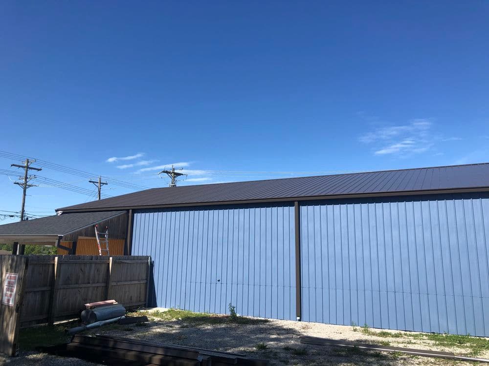 Metal building with blue siding and clear sky, located near utility poles and a wooden fence.