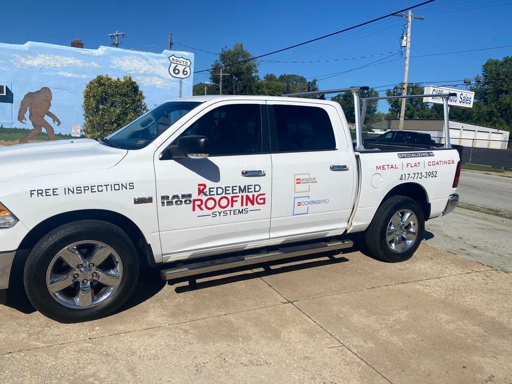 White pickup truck with "Redeemed Roofing Systems" signage, parked near a Route 66 mural.