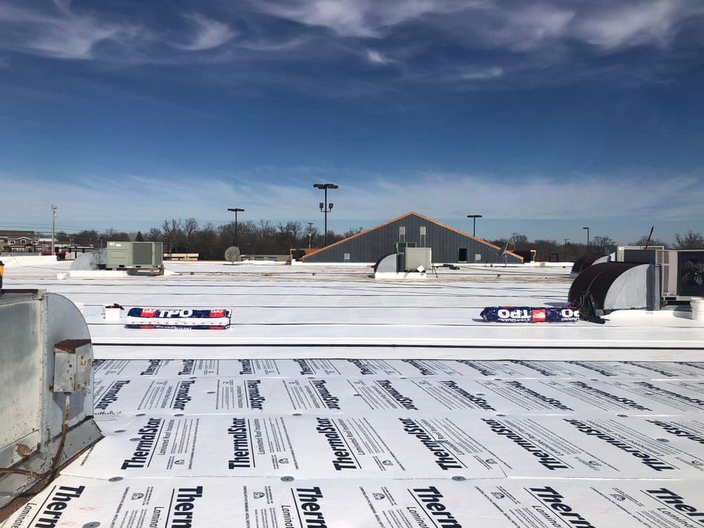 Flat commercial roof installation with white membrane, HVAC units, and clear blue sky.