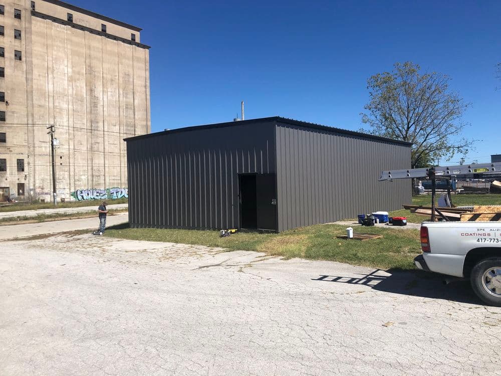 New metal storage building near an industrial site with clear blue sky and workers.