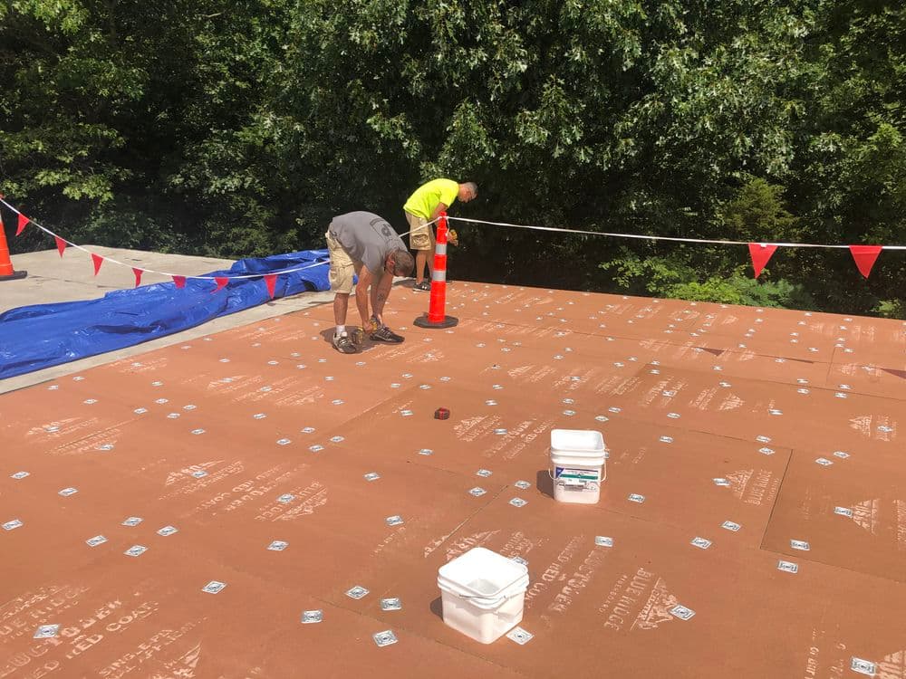 Workers installing roofing materials on a construction site with safety cones and tarps.