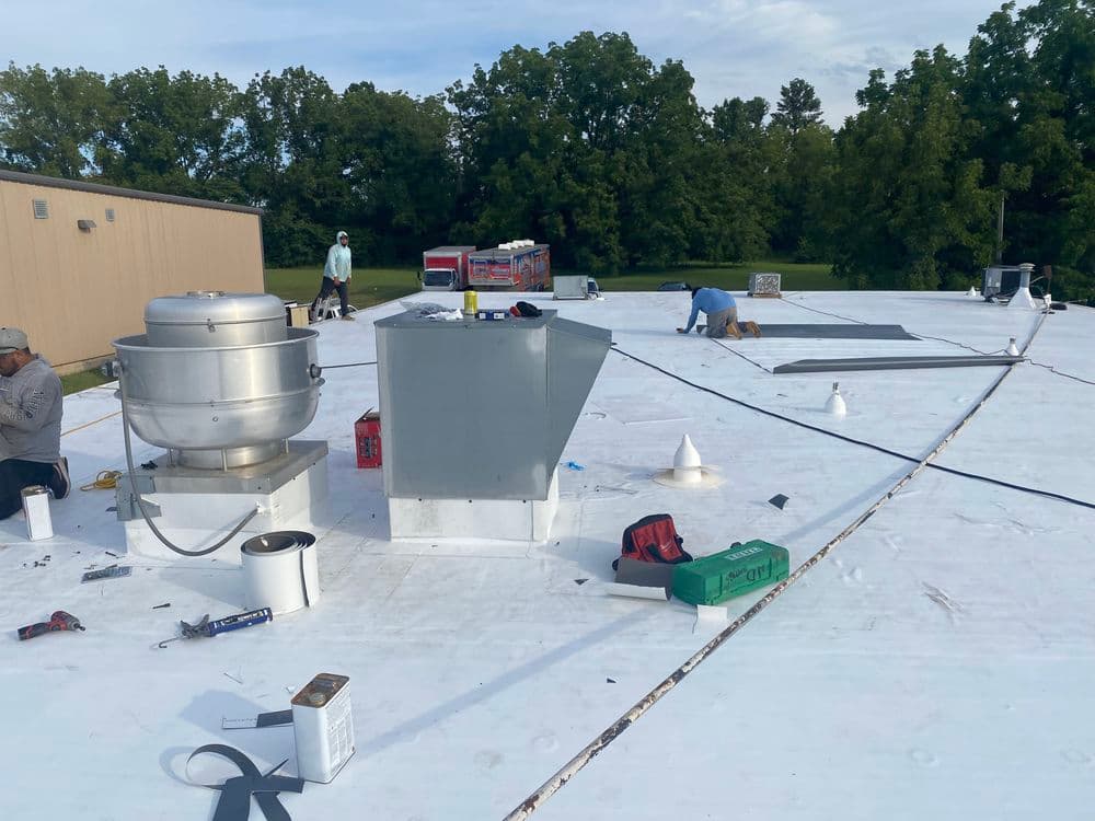 Roof repair workers installing equipment on a commercial building's flat roof.