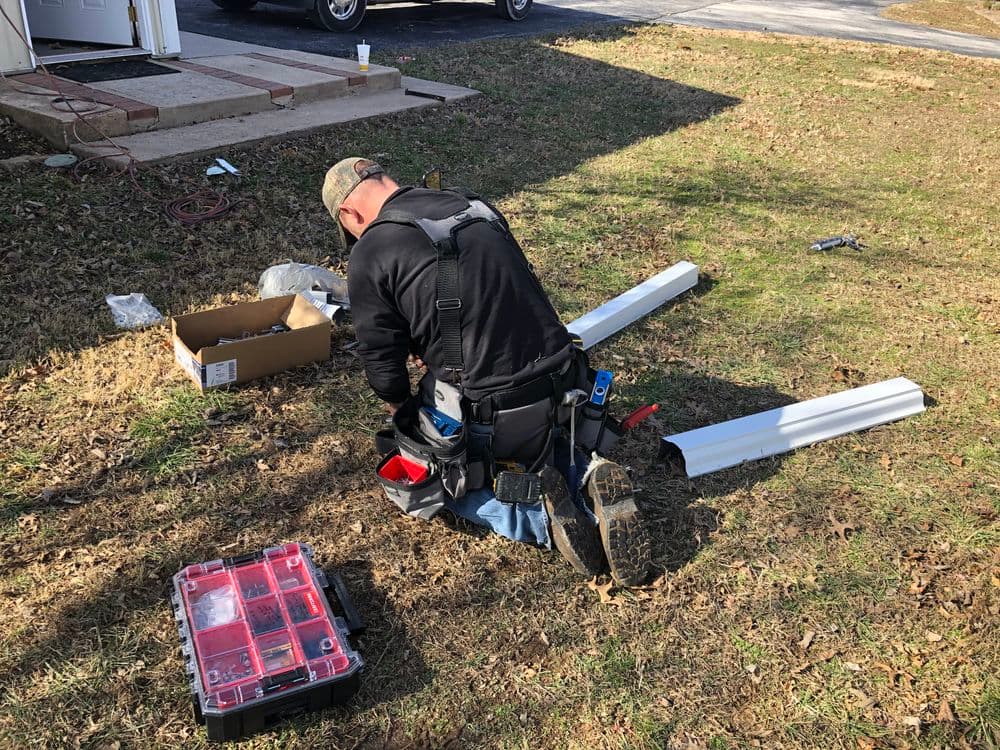 Worker installing outdoor equipment on grassy area with tools and boxes nearby.