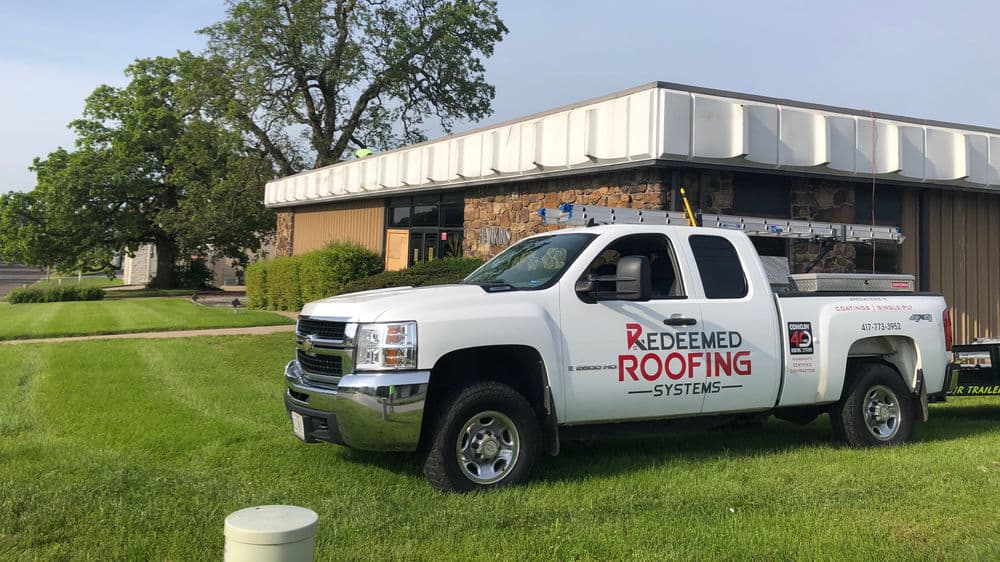 Redeemed Roofing Systems truck parked in front of a commercial building for roofing services.